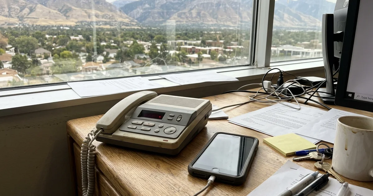 Old answering machine next to a modern phone on a desk