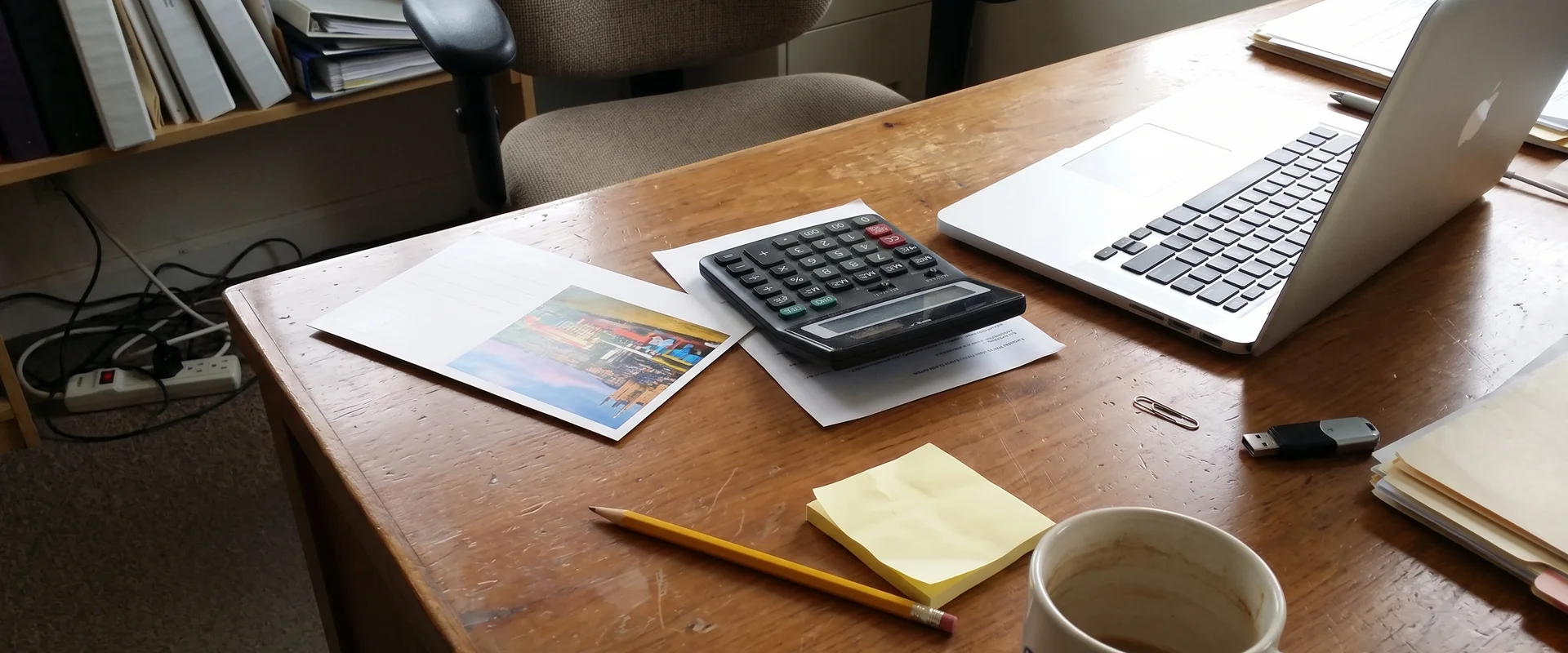 Calculator and postcard on a desk next to a laptop