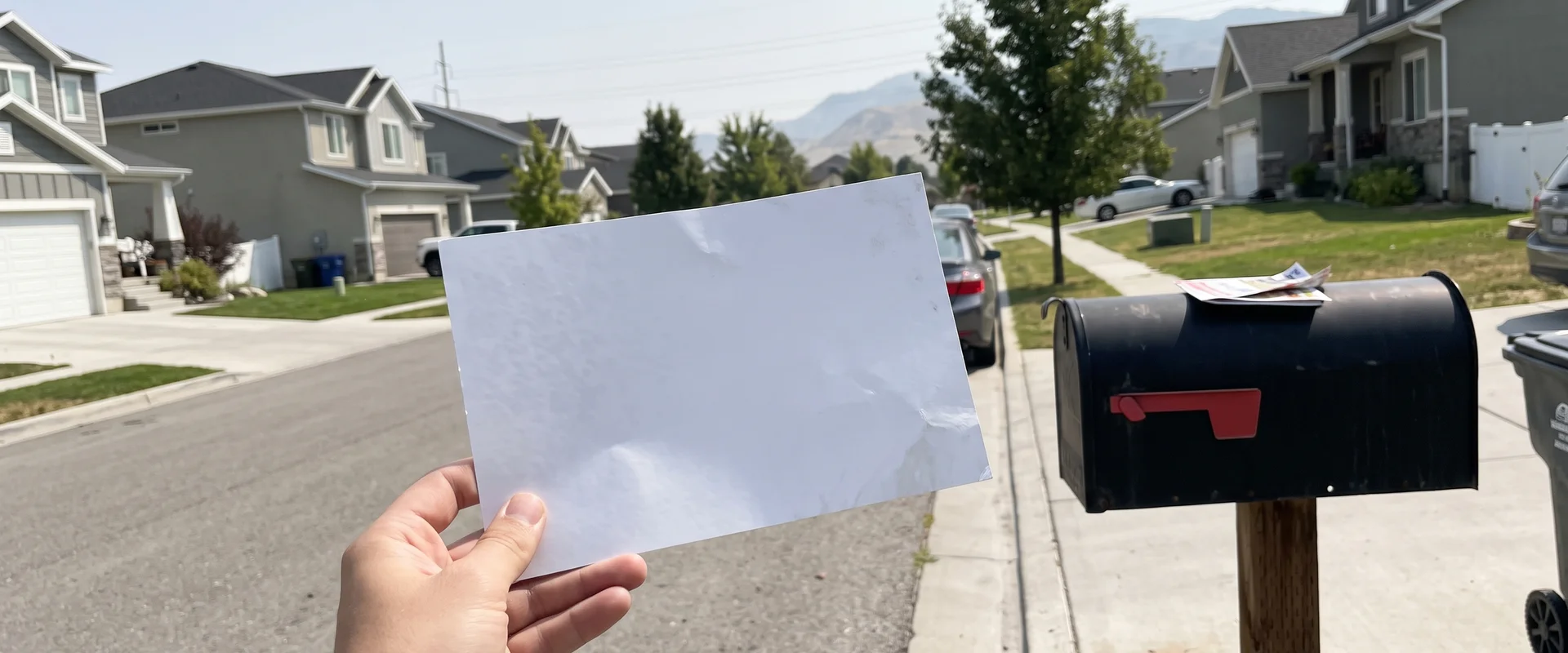 Oversized shared Community Postcard held next to a curbside mailbox on a Draper street