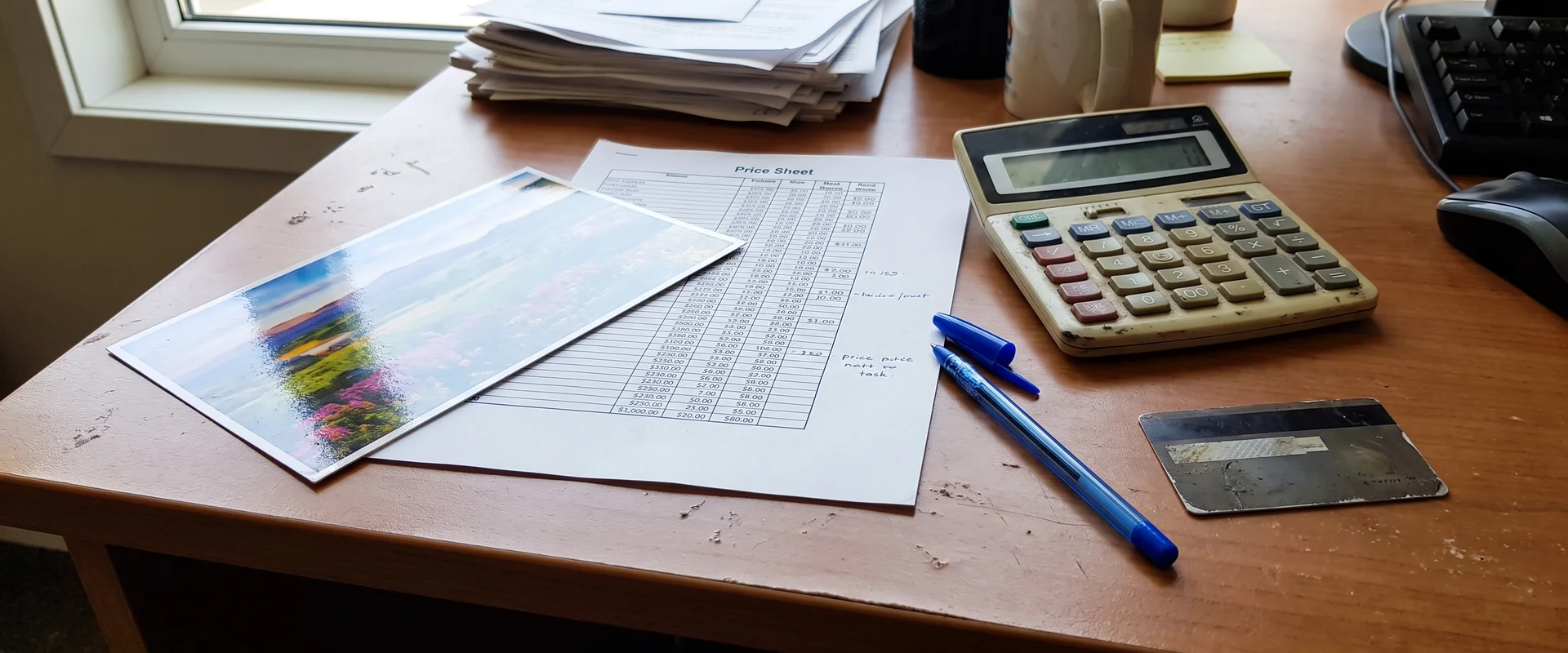 Postcard, price sheet and calculator on a small business desk